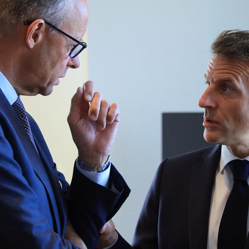 Bundeskanzler Merz und Frankreichs Präsident Macron stehen sich gegenüber und sprechen vertraulich miteinander.