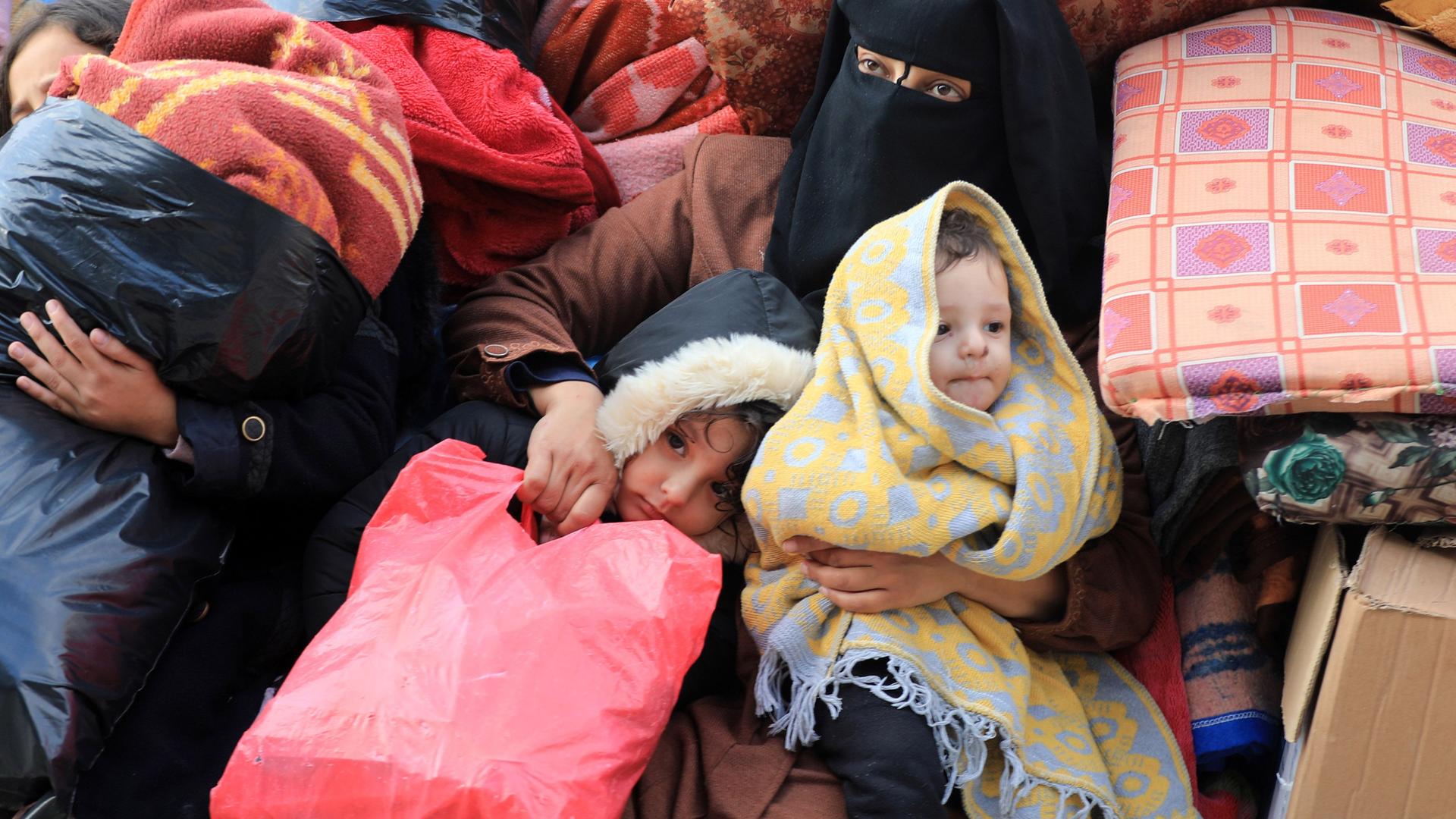 Eine vollverschleierte Frau mit ihren beiden Kindern in Decken eingehüllt und auf gepackten Sachen.