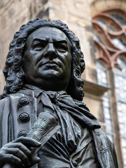 Blick auf den Kopf der Statue von Johann Sebastian Bach vor der Thomaskirche Leipzig, die ihn mit Perrücke und Notenrolle in der Hand zeigt.