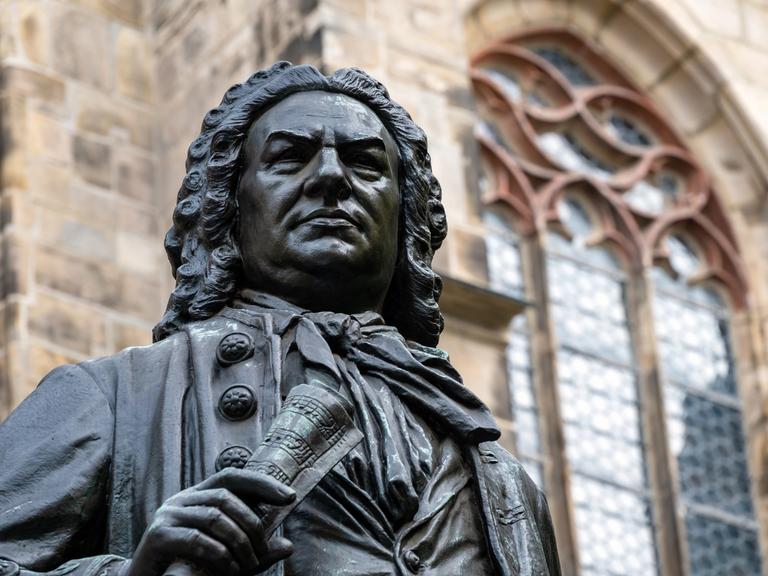 Blick auf den Kopf der Statue von Johann Sebastian Bach vor der Thomaskirche Leipzig, die ihn mit Perrücke und Notenrolle in der Hand zeigt.