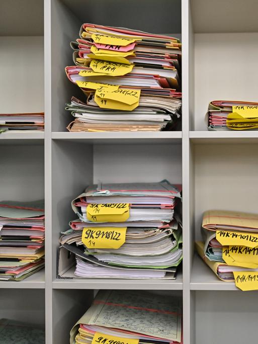 Mehrere Stapel mit Akten liegen in einem Regal.