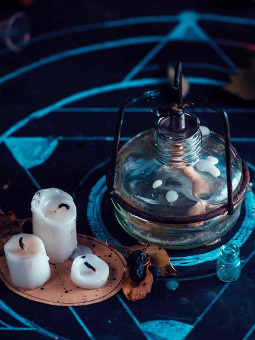 Stillleben: Arbeitsplatz eines Alchemisten mit Bunsenbrenner, Kerzen und Kreide-Pentagramm.