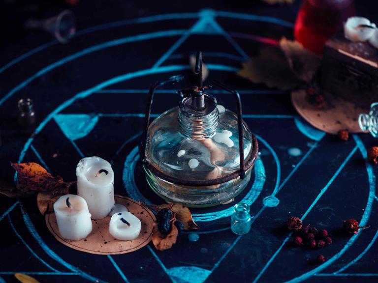 Stillleben: Arbeitsplatz eines Alchemisten mit Bunsenbrenner, Kerzen und Kreide-Pentagramm.