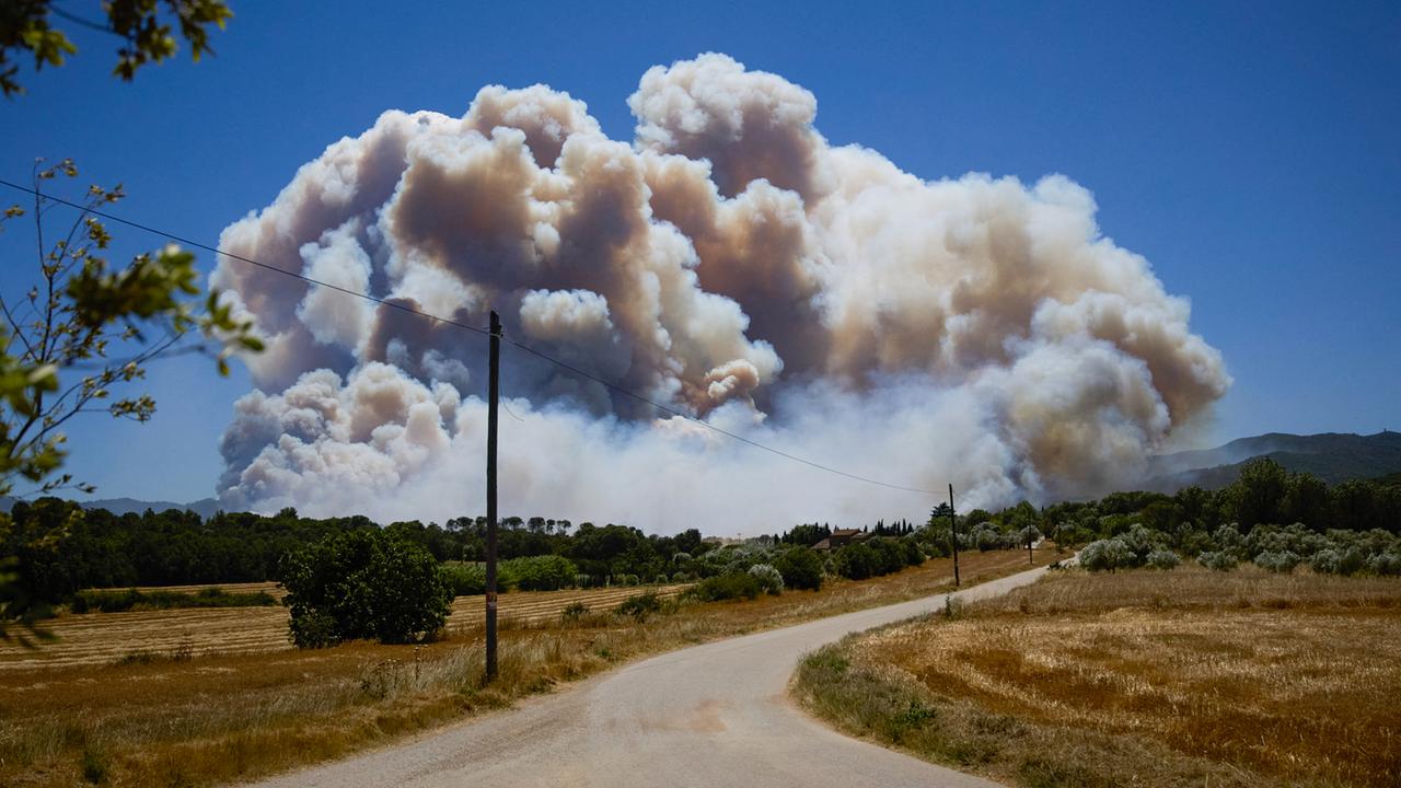 Über einer ausgetrockneten Landschaft ragt in der Ferne der Rauch eines großen Feuers auf.