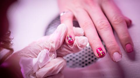 Zu sehen ist eine Nahaufnahme einer Behandlung in einem Nagelstudio. Bunter Nagellack wird auf Fingernägel aufgetragen.
