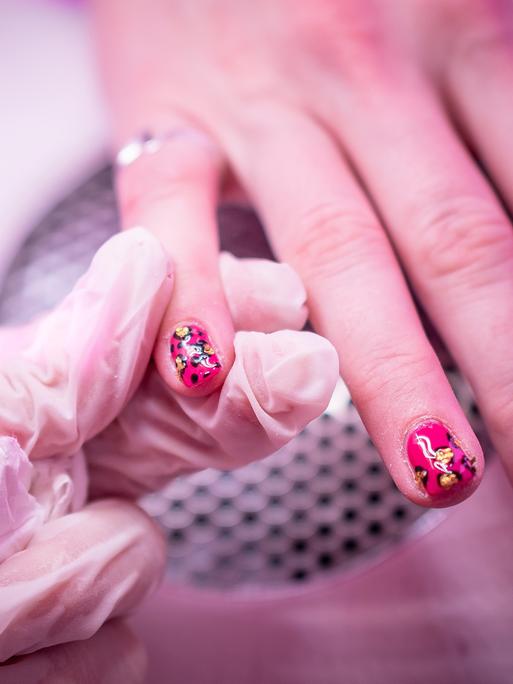 Zu sehen ist eine Nahaufnahme einer Behandlung in einem Nagelstudio. Bunter Nagellack wird auf Fingernägel aufgetragen. Zu sehen ist eine Nahaufnahme einer Behandlung in einem Nagelstudio. Bunter Nagellack wird auf Fingernägel aufgetragen.