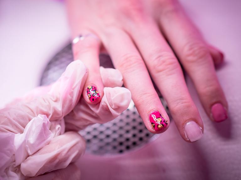 Zu sehen ist eine Nahaufnahme einer Behandlung in einem Nagelstudio. Bunter Nagellack wird auf Fingernägel aufgetragen. Zu sehen ist eine Nahaufnahme einer Behandlung in einem Nagelstudio. Bunter Nagellack wird auf Fingernägel aufgetragen.
