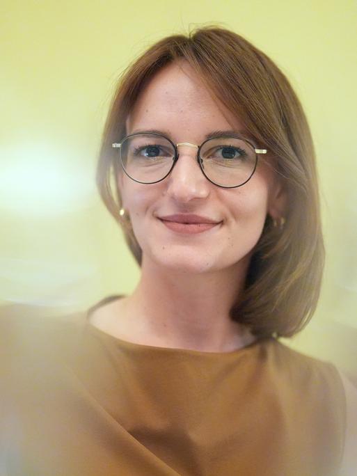 Jehona Kicaj lächelt in die Kamera. Sie trägt eine Brille und einen mittelbraunen Bob.