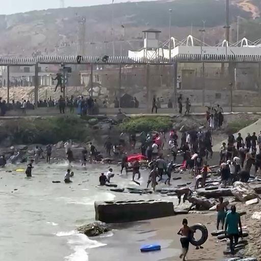 Menschen steigen, teils mit Schwimmreifen, am Strand der spanischen Exklave Ceuta aus dem Wasser.