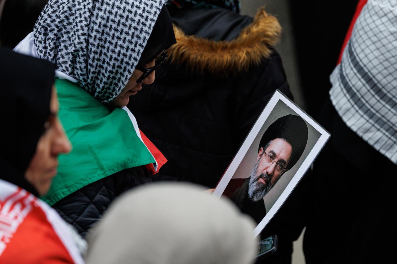 Das Bild zeigt mehrere Demonstrantinnen mit Kopftüchern in der Nahaufnahme. Eine von ihnen hält das kleine Foto in der Hand und schaut darauf. 