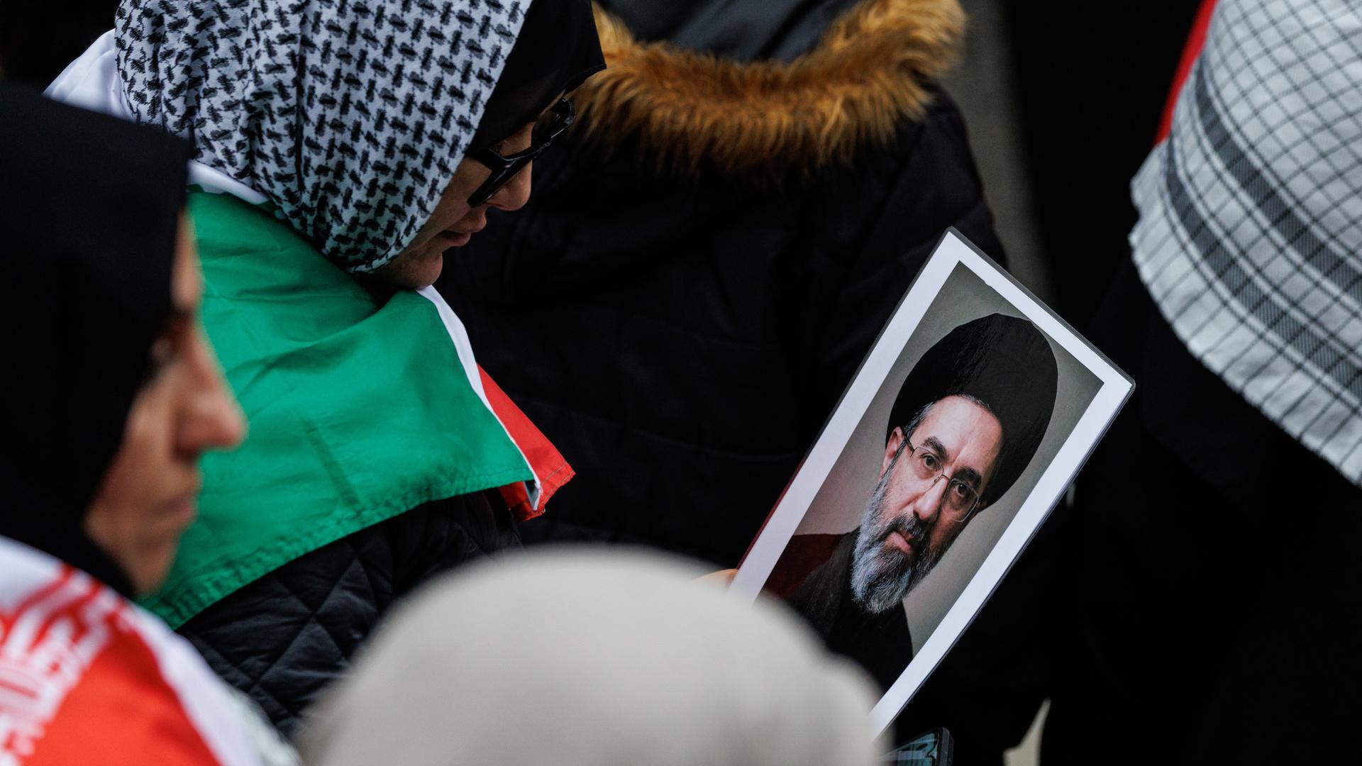 Das Bild zeigt mehrere Demonstrantinnen mit Kopftüchern in der Nahaufnahme. Eine von ihnen hält das kleine Foto in der Hand und schaut darauf. Das Bild zeigt mehrere Demonstrantinnen mit Kopftüchern in der Nahaufnahme. Eine von ihnen hält das kleine Foto in der Hand und schaut darauf.