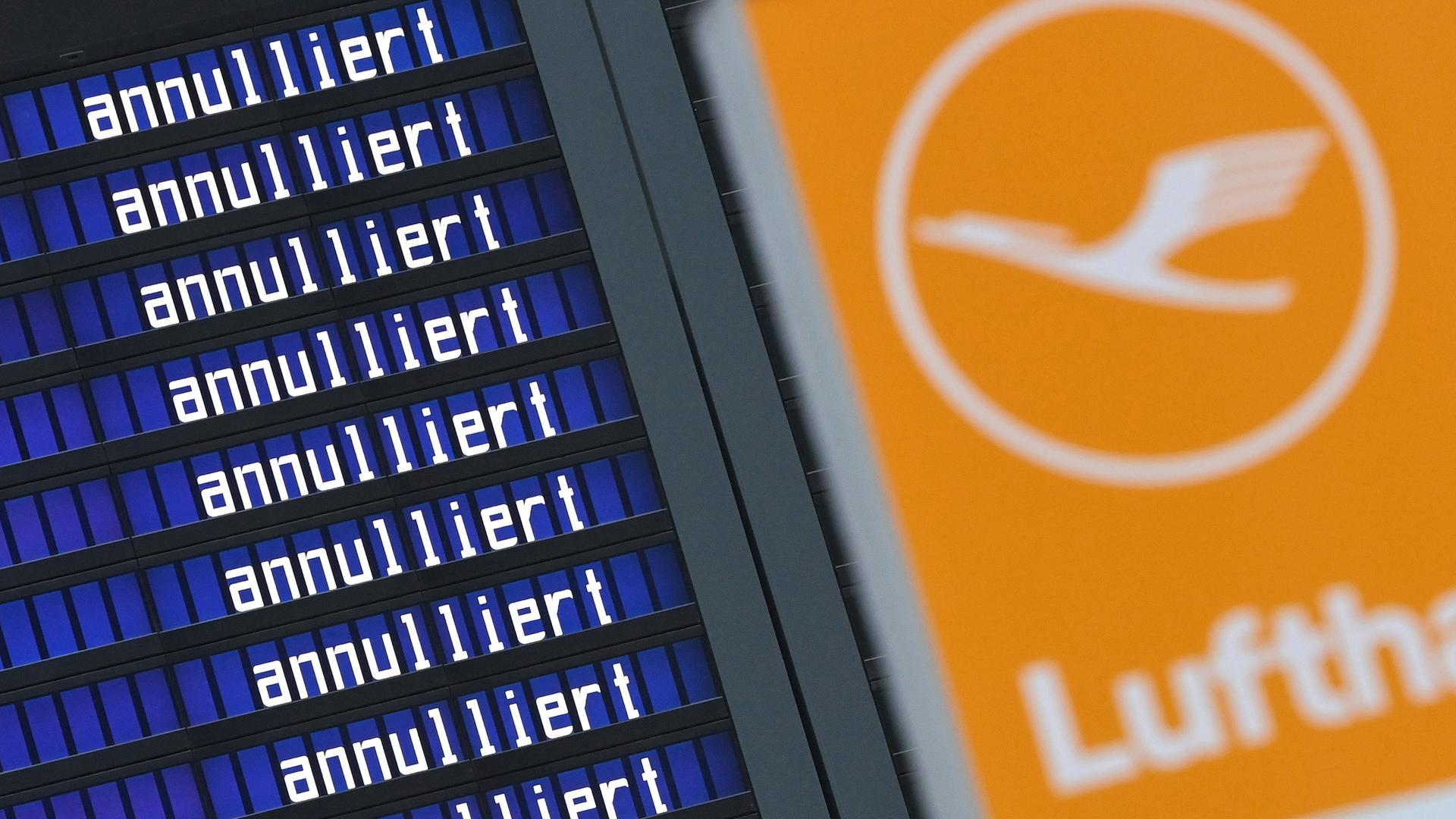 Eine Anzeigetafel mit der sich wiederholenden Aufschrift "annulliert". Daneben das Logo der Lufthansa mit einem Kranich.