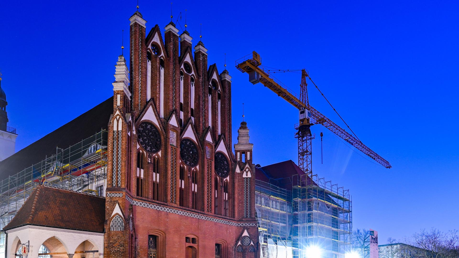 Ein Baukran steht am frühen Morgen neben einem Gerüst an der südlichen Fassade des Rathauses von Frankfurt Oder.