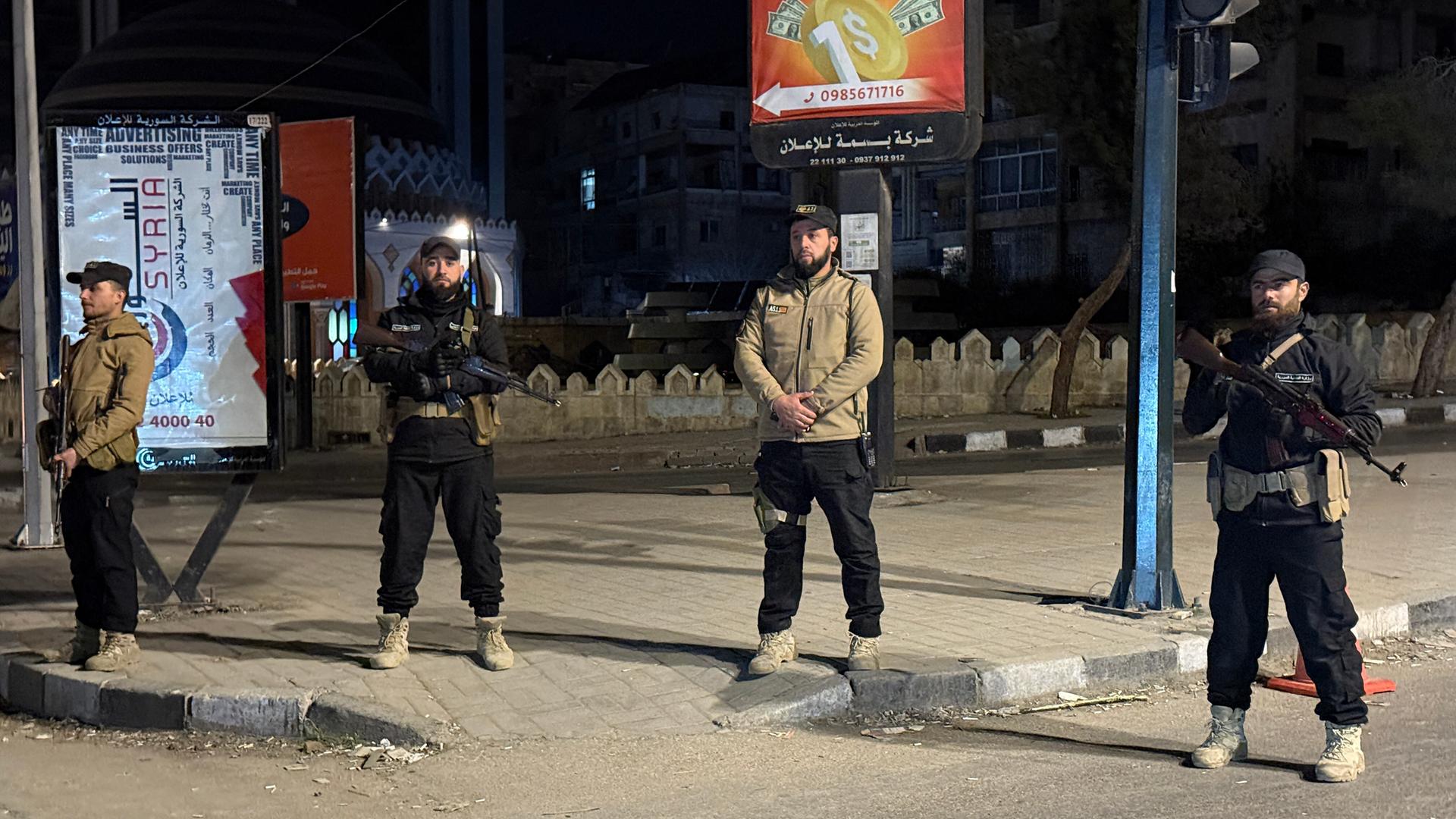 Vier Männer stehen im Dunkeln auf einer Straße, sie gehören zur syrischen Regierung. Einige tragen Gewehre. 