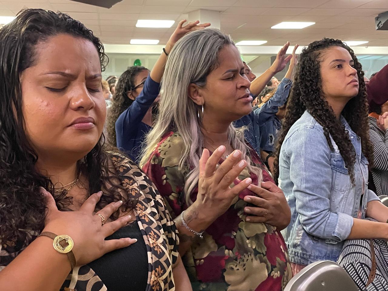 Mehrere nebeinander sitzende junge Frauen mit geschlossenen Augen und die Hände an der Brust beten konzentriert.