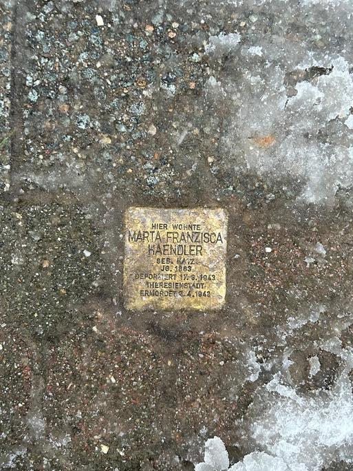 Hände mit Kelle und Zement setzen einen Stolperstein in den Boden. Die Steine erinnern an Personen, die von den Nazis deportiert und umgebracht wurden (Symbolbild).