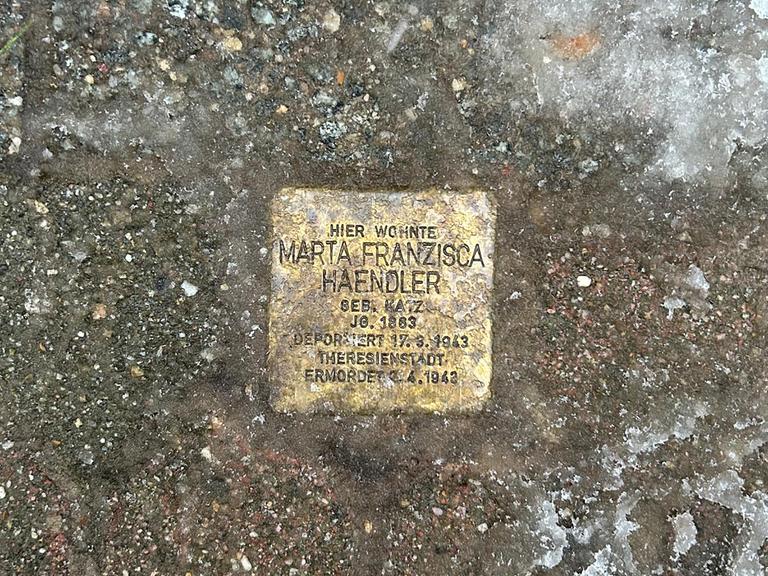 Hände mit Kelle und Zement setzen einen Stolperstein in den Boden. Die Steine erinnern an Personen, die von den Nazis deportiert und umgebracht wurden (Symbolbild).