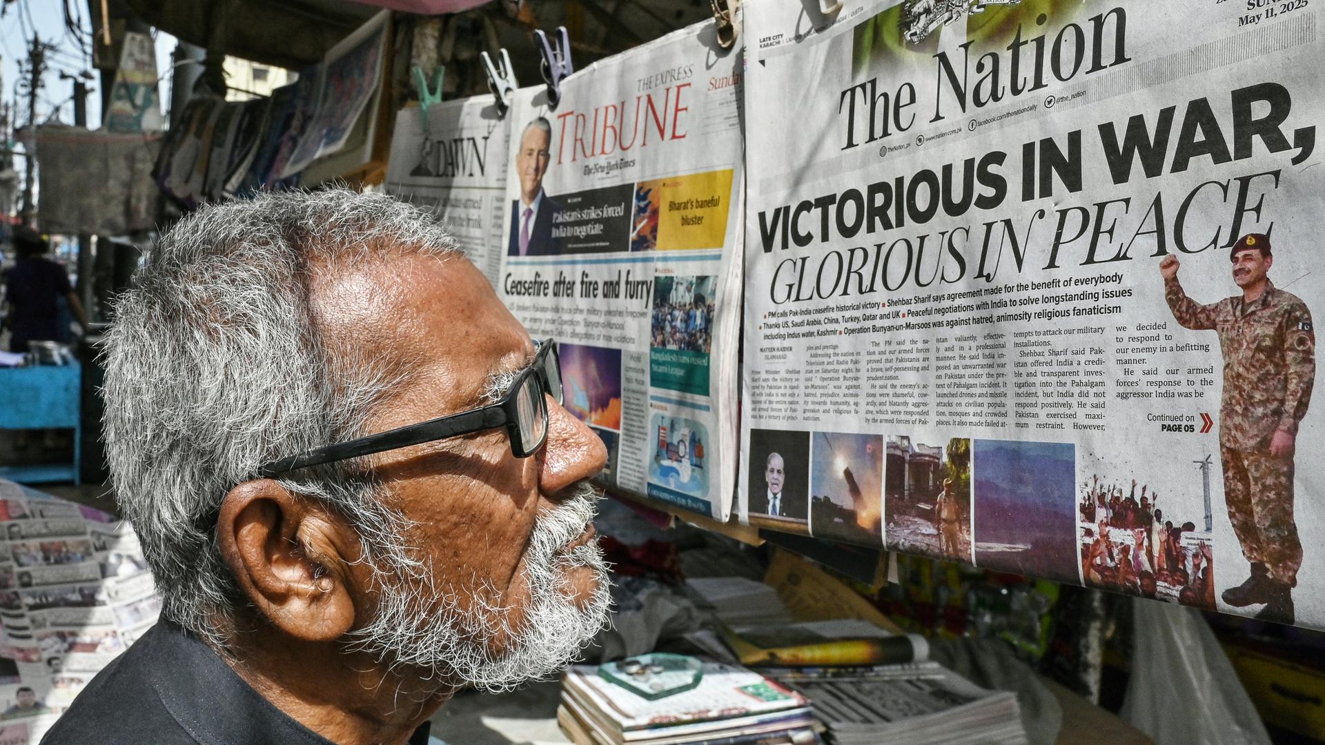 Ein Mann steht in der Stadt Karachi in Pakistan vor einem Zeitungsstand. Er liest eine Zeitung, die dort hängt. Auf dem Titelblatt steht auf englisch "Siegreich im Krieg - Glorreich im Frieden". Ein Mann steht in der Stadt Karachi in Pakistan vor einem Zeitungsstand. Er liest eine Zeitung, die dort hängt. Auf dem Titelblatt steht auf englisch "Siegreich im Krieg - Glorreich im Frieden".