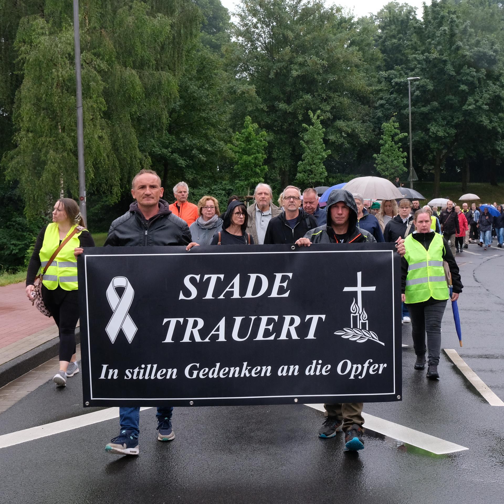 Viele Menschen laufen hinter einem schwarzen Banner. Es trägt in weißen Buchstaben die Aufschrift: "Stade trauert. In stillem Gedenken an die Opfer."