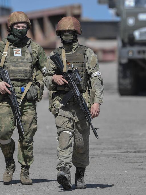 Zwei russische Soldaten in der Region Cherson, im Hintergrund ein Militärfahrzeug mit dem Z-Symbol.