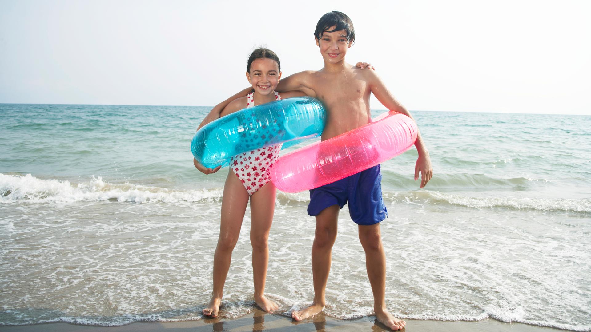 Junge und Mädchen (8–10) am Strand, mit Schwimmringen, Porträt Junge und Mädchen (8–10) am Strand, mit Schwimmringen, Porträt