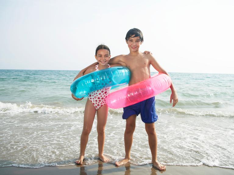 Junge und Mädchen (8–10) am Strand, mit Schwimmringen, Porträt