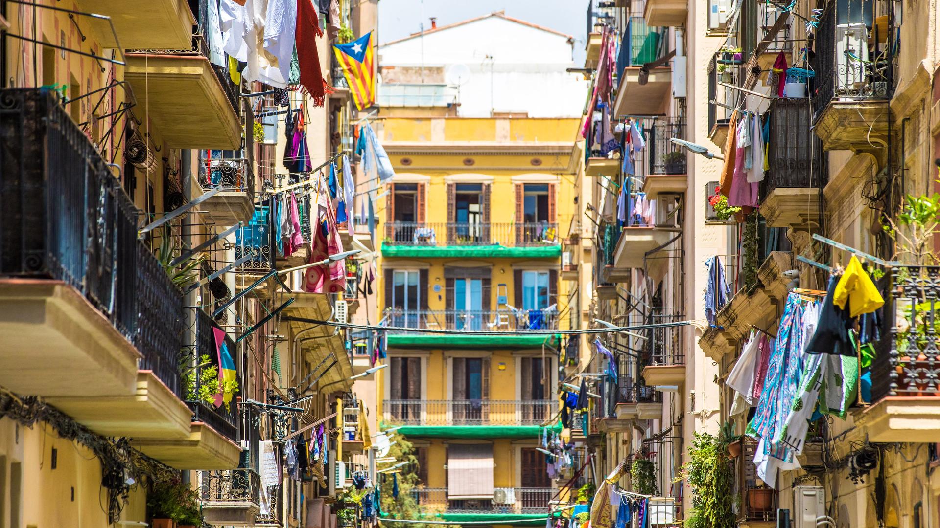 Blick in eine Straße mit mehrstöckigen Wohnhäusern. Auf den Balkonen hängt viel Wäsche zum trocknen.