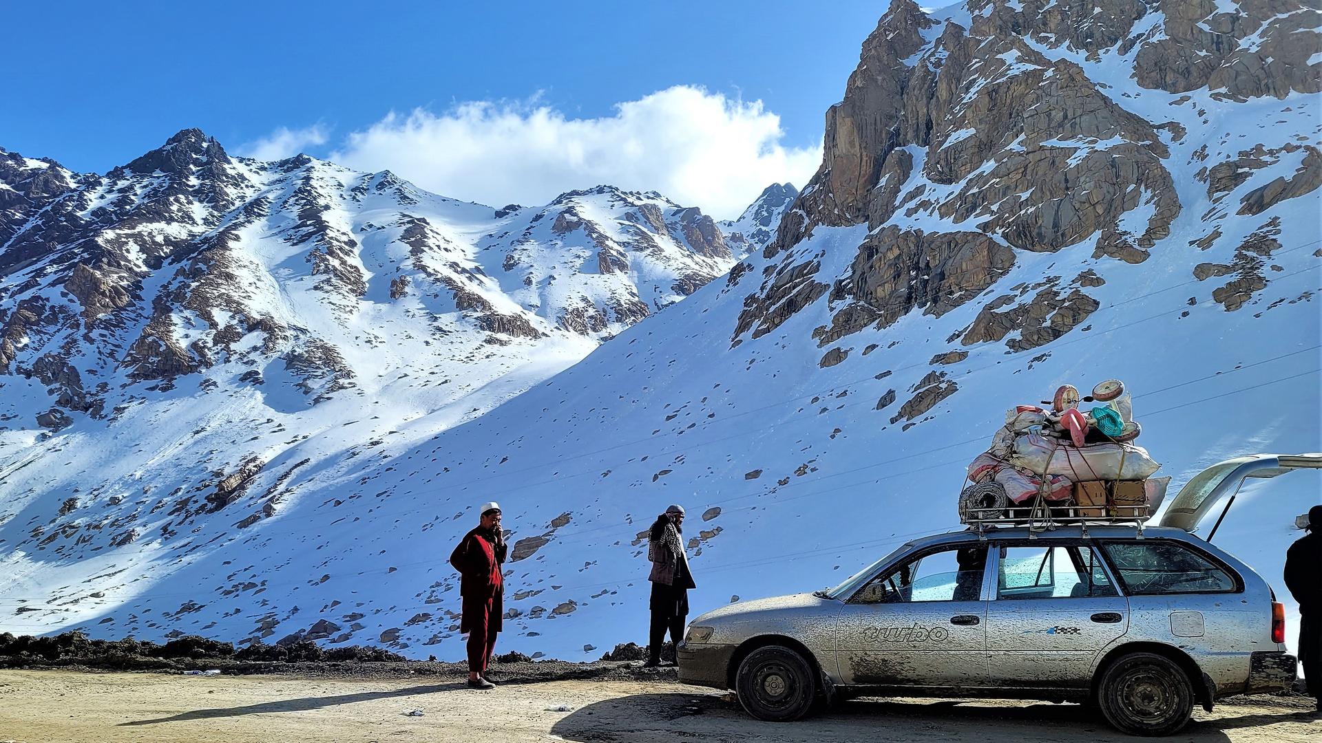 Auf einer Gebirgsstraße im schneebedeckten Hindukusch steht ein altes Auto mit viel Gepäck auf dem Dach, das von Taliban kontrolliert wird. Auf einer Gebirgsstraße im schneebedeckten Hindukusch steht ein altes Auto mit viel Gepäck auf dem Dach, das von Taliban kontrolliert wird.