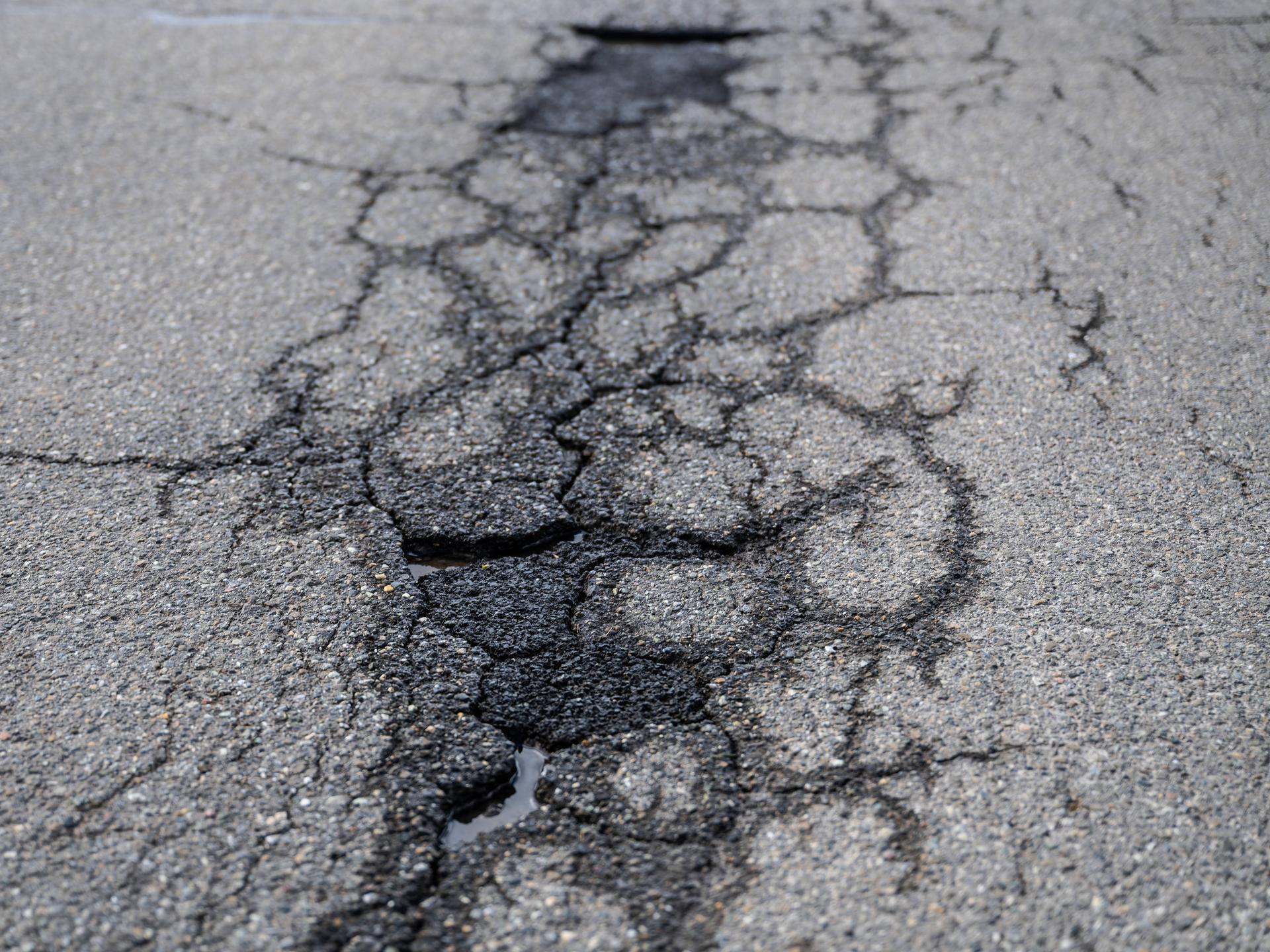 Risse und Schlaglöcher auf einer asphaltierten Straße. 