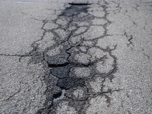 Risse und Schlaglöcher auf einer asphaltierten Straße. 