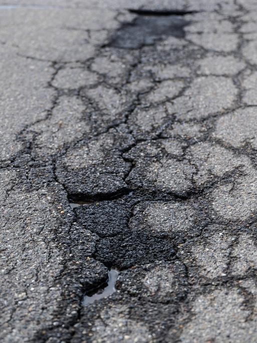 Risse und Schlaglöcher auf einer asphaltierten Straße. 