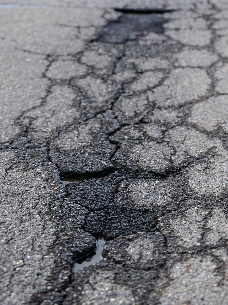 Risse und Schlaglöcher auf einer asphaltierten Straße. 