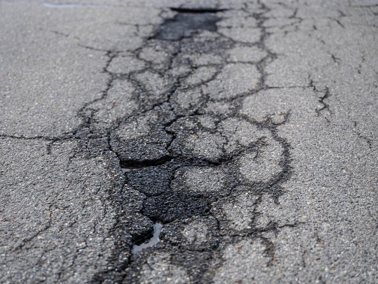 Risse und Schlaglöcher auf einer asphaltierten Straße. 