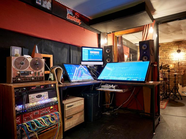 Einrichtung eines Tonstudios mit Bildschirmen, Lautsprechern und Patchfeldern mit Kabelverbindungen.