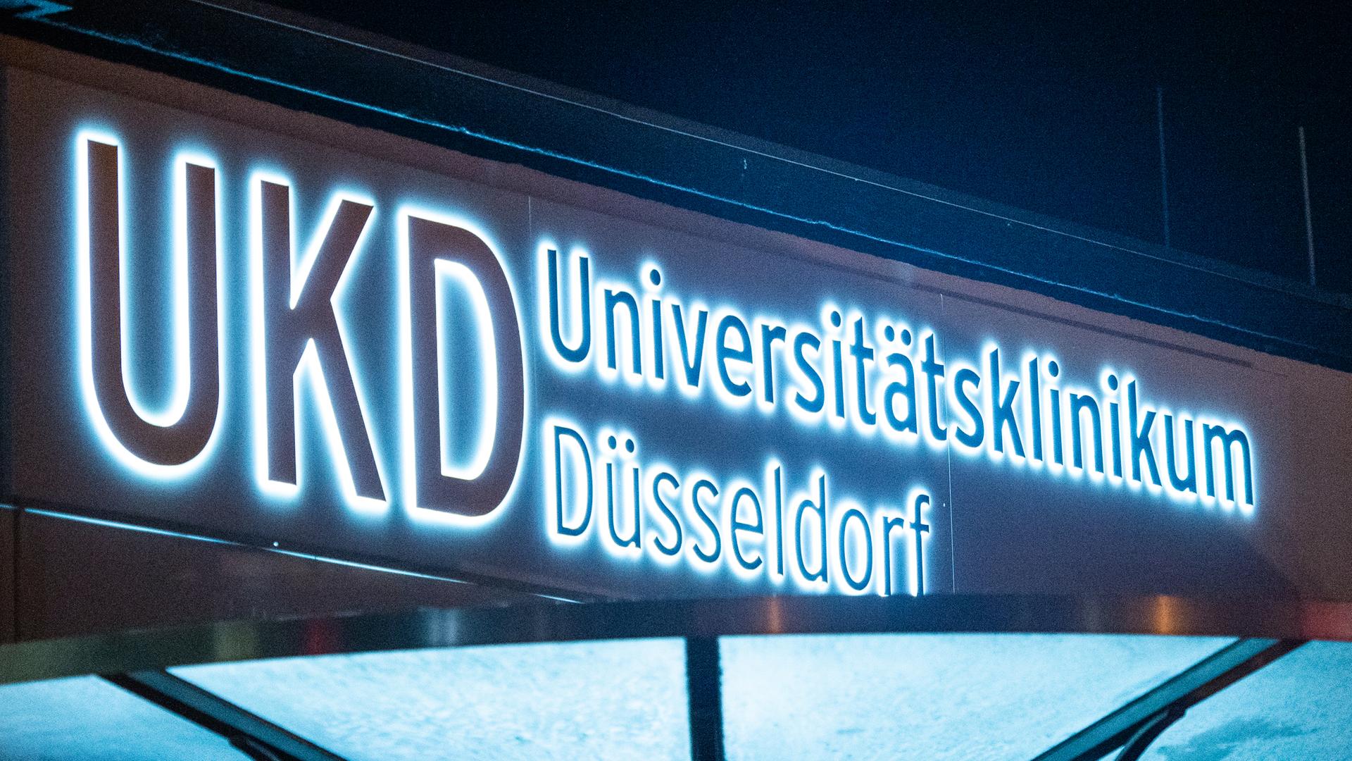 Das Logo des Universitätsklinikums Düsseldorf UKD leuchtet an einem Eingang des Krankenhauses.