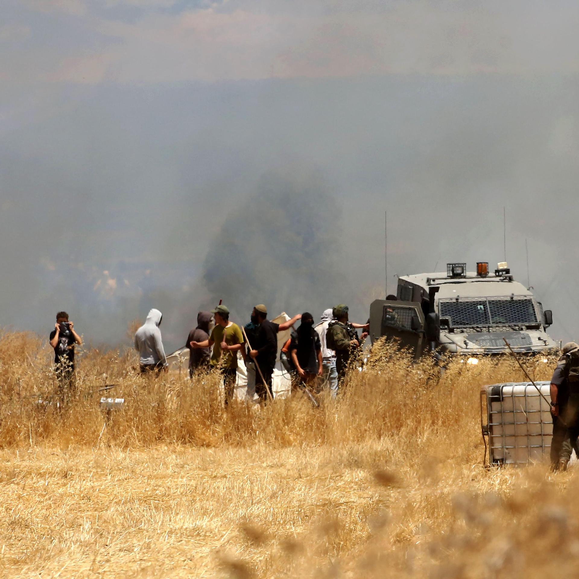 In der Nähe von Nablus gab es erneut Gewalt zwischen israeIischen Siedlern und Palästinensern. Menschen stehen auf einem Feld, dahinter steigt Rauch auf.