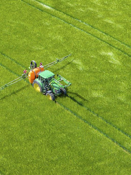 Drohnenfoto eines düngenden Traktors auf einem grünen Feld