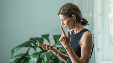 Eine Frau schaut konzentriert auf ein Handy und trägt Kopfhörer.