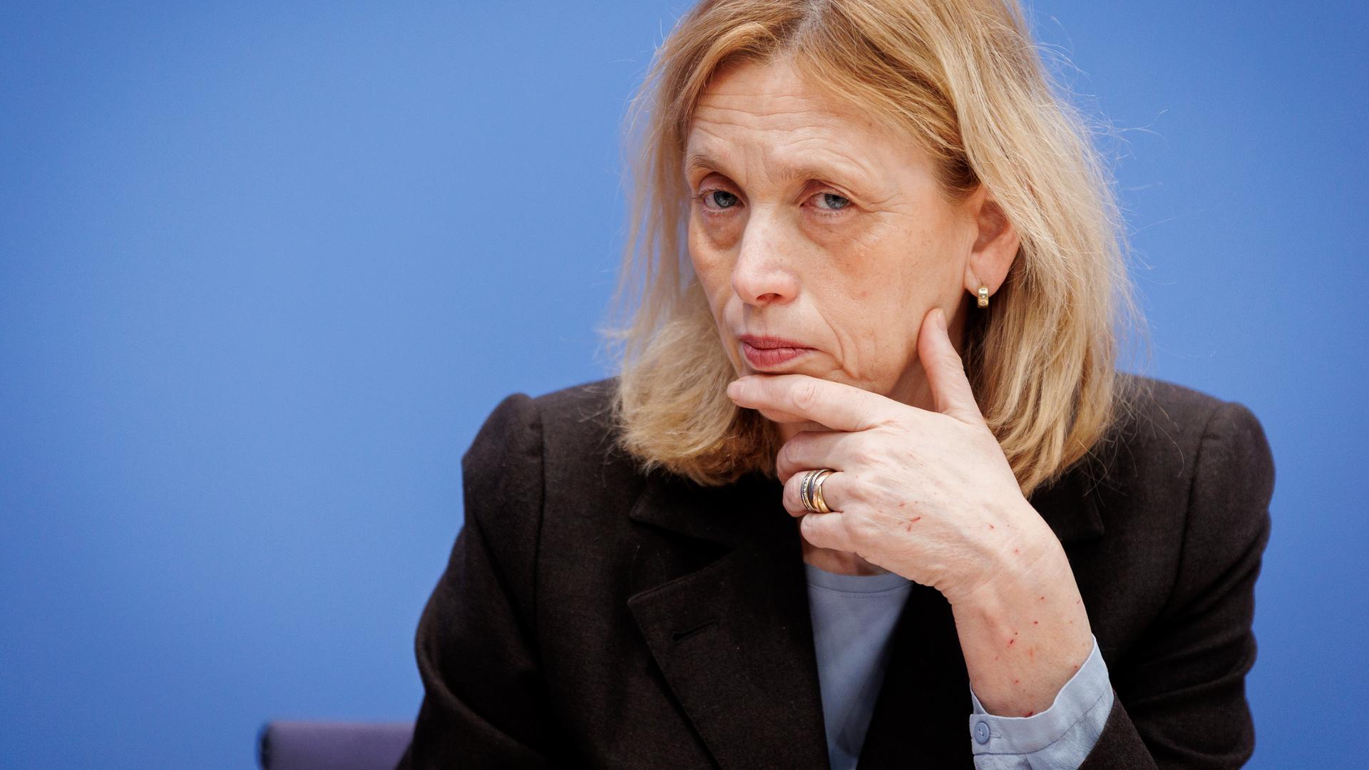Karin Prien stützt bei einer Bundespressekonferenz den Kopf auf der Hand auf und schaut prüfend ins Publikum.