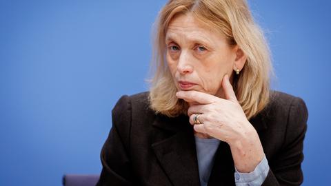 Karin Prien stützt bei einer Bundespressekonferenz den Kopf auf der Hand auf und schaut prüfend ins Publikum.