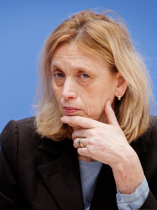 Karin Prien stützt bei einer Bundespressekonferenz den Kopf auf der Hand auf und schaut prüfend ins Publikum.