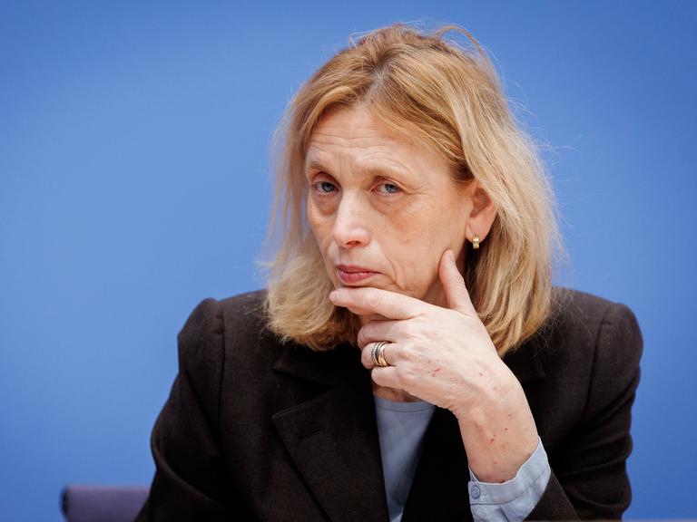 Karin Prien stützt bei einer Bundespressekonferenz den Kopf auf der Hand auf und schaut prüfend ins Publikum.