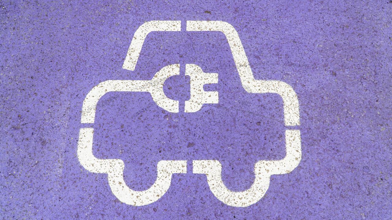 Nahaufnahme eines weißen Symbols für Elektrofahrzeuge, das auf eine violette Asphaltoberfläche gemalt ist