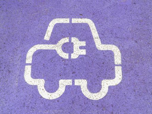 Nahaufnahme eines weißen Symbols für Elektrofahrzeuge, das auf eine violette Asphaltoberfläche gemalt ist Nahaufnahme eines weißen Symbols für Elektrofahrzeuge, das auf eine violette Asphaltoberfläche gemalt ist