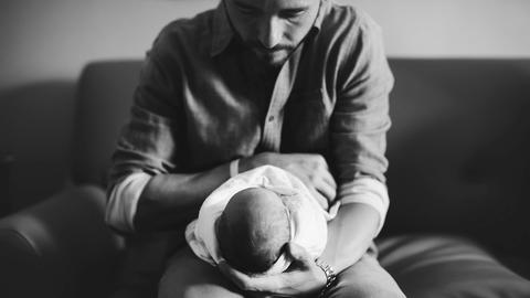 Ein Vater hat sein neugeborenes Kind auf seinem Schoß und schaut es an.