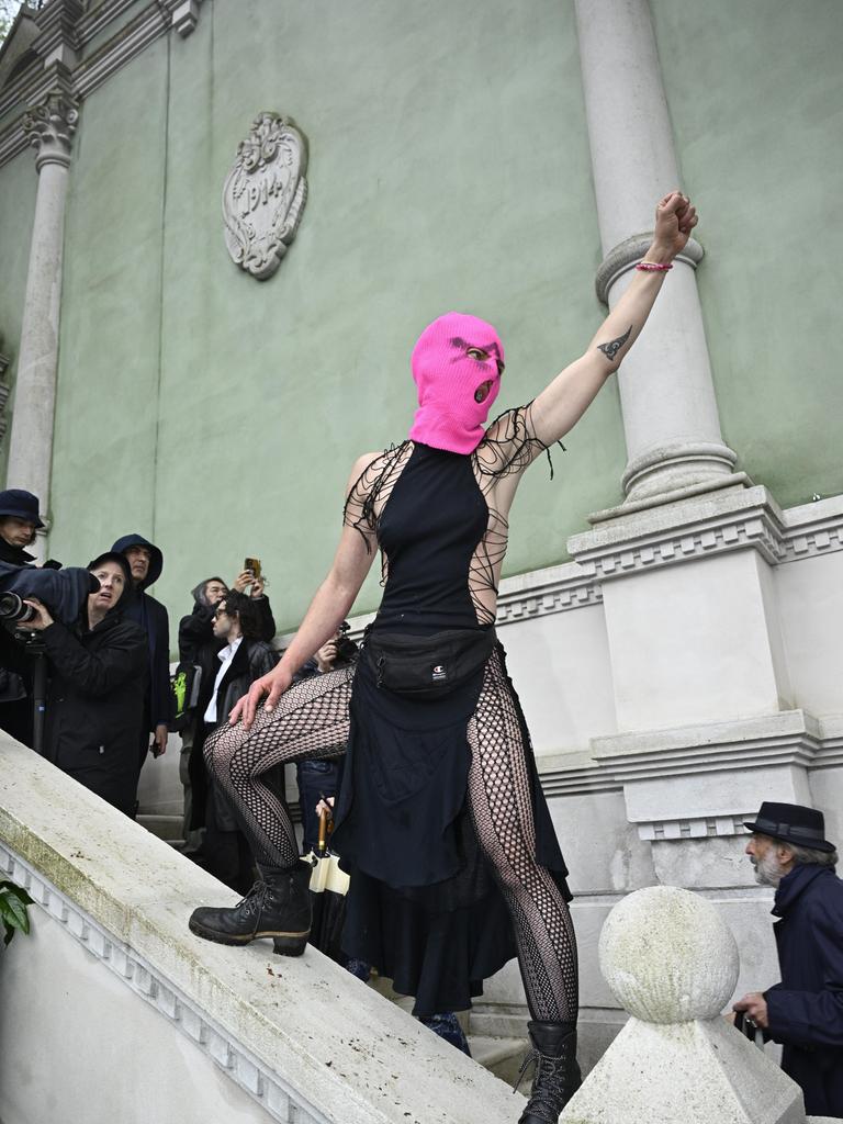 Eine Frau mit knallpinker Strickmaske steht auf dem steinernden Treppengeländer vor dem russischen Pavillon auf der Biennale in Venedig, reckt ihre Faust in die Luft und schreit.