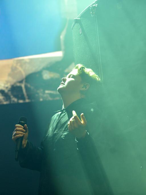 Kae Tempest steht bei einem Auftritt auf der Bühne, hat die Augen geschlossen und den Kopf nach oben gedreht, in Richtung eines grünen Lichtstrahls von der Decke.