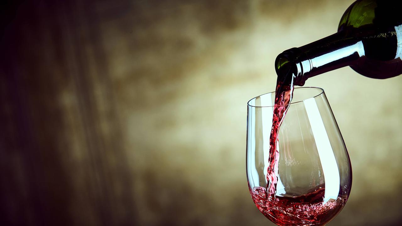 Rotwein wird aus einer Flasche in ein Weinglas gefüllt