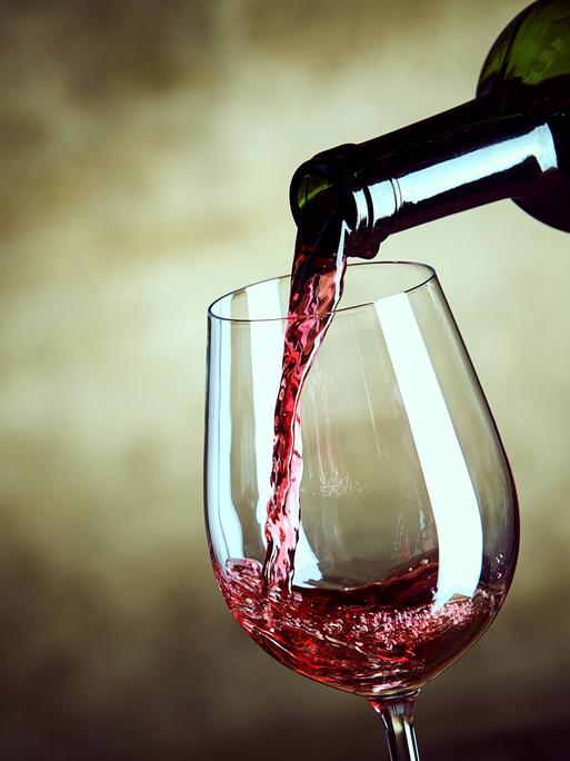 Rotwein wird aus einer Flasche in ein Weinglas gefüllt