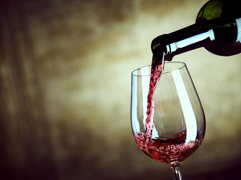 Rotwein wird aus einer Flasche in ein Weinglas gefüllt